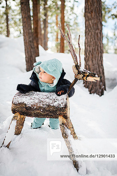 Baby boy ankle deep in forest snow leaning against wooden deer  South Lake Tahoe  California  USA