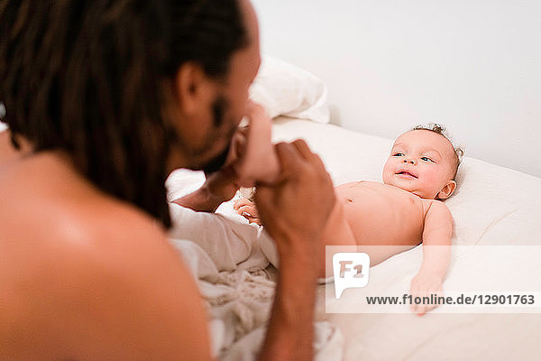 Father kissing baby son's bare feet on bed