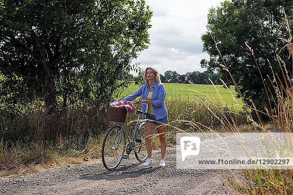 Mature woman pushing bicycle along rural road