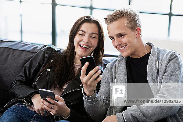 Teenager  Mädchen und Junge sitzen auf dem Sofa und schauen auf ein Smartphone