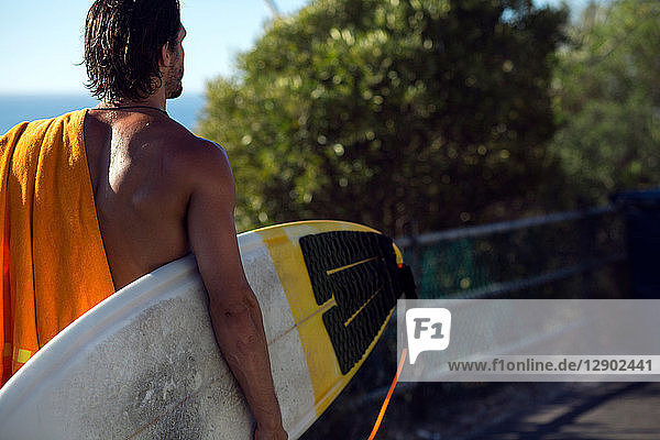 Mittelgroßer erwachsener männlicher Surfer mit Surfbrett am Strandweg  Rückansicht  Camps Bay Beach  Kapstadt  Südafrika