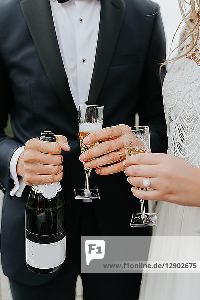 Braut und Bräutigam halten Champagnerflasche und Flöten