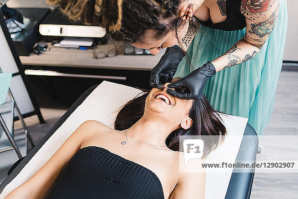 Tätowierer durchbohrt die Nase eines Kunden im Salon