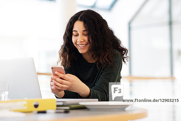 Teenager-Schülerin am Klassenzimmer-Schreibtisch mit Blick auf Smartphone