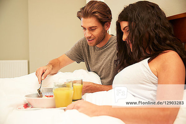 Ehepaar beim Frühstück mit Obst und Orangensaft im Bett