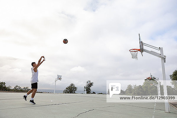 Männlicher jugendlicher Basketballspieler wirft Ball in Richtung Basketballkorb