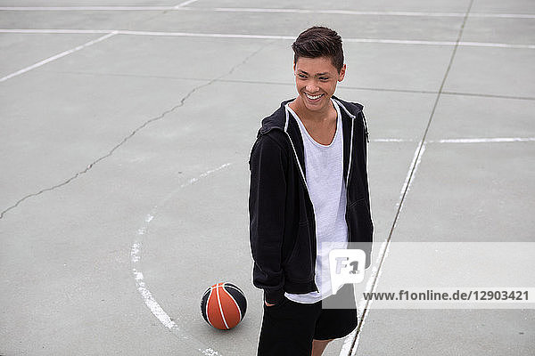 Männlicher jugendlicher Basketballspieler auf Basketballfeld  lächelnd