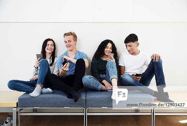 Vier Gymnasiasten auf Sitzgelegenheiten mit Blick auf Smartphones