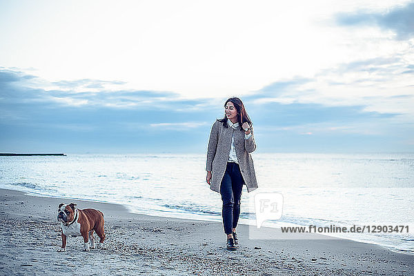 Junge Frau geht mit Hund am Strand spazieren