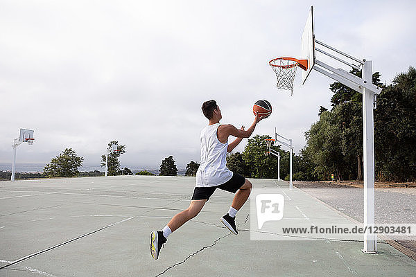 Männlicher jugendlicher Basketballspieler springt mit dem Ball in Richtung Basketballkorb