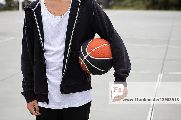 Männlicher jugendlicher Basketballspieler auf Basketballfeld mit Ball unter dem Arm  Mittelteil