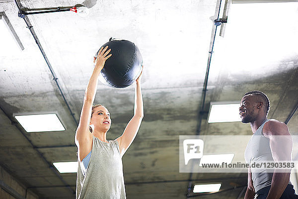 Trainer beobachtet weiblichen Klienten beim Heben eines Medizinballs im Fitnessstudio