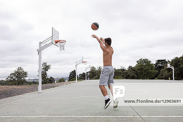 Männlicher jugendlicher Basketballspieler springt und wirft Ball in Richtung Basketballkorb