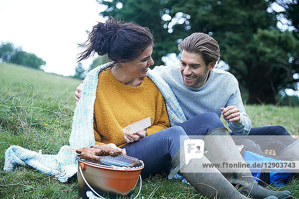 Couple sitting in rural field cooking on barbecue grill