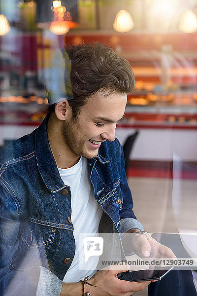 Male student looking at smartphone in cafe window seat  view through window