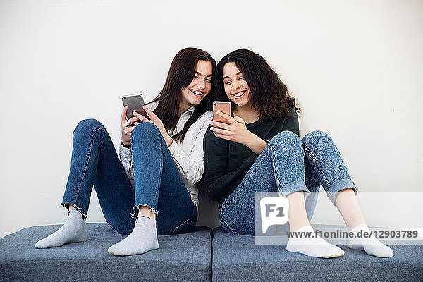 Zwei Highschool-Mädchen auf Sitzgelegenheiten mit Blick auf Smartphones