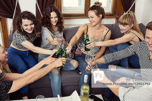Gruppe von erwachsenen Freunden und Freundinnen  die auf dem Sofa sitzen und einen Toast aussprechen