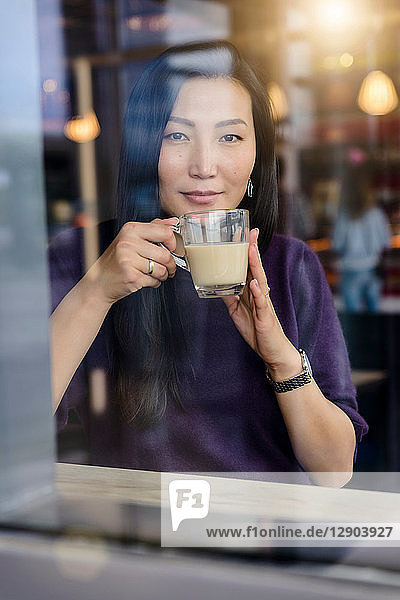 Mittelgroße erwachsene Frau beim Kaffeetrinken am Fensterplatz eines Cafés  Porträt