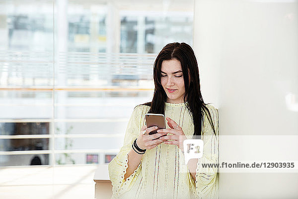 High-School-Mädchen in der Schullobby schaut auf Smartphone