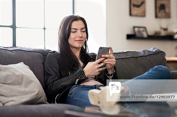 Teenagerin sitzt auf Sofa und schaut auf Smartphone