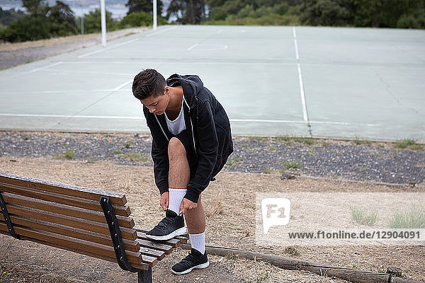 Männlicher jugendlicher Basketballspieler beim Befestigen von Turnschuhen am Basketballfeld