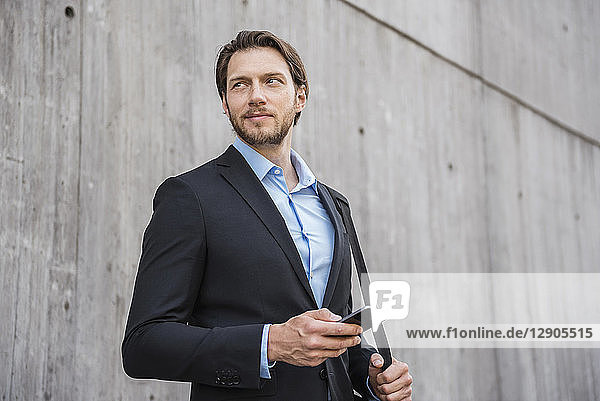 Businessman standing at concrete wall holding smartphone