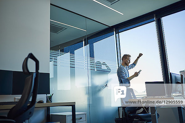 Businessman in office using cell phone at the window