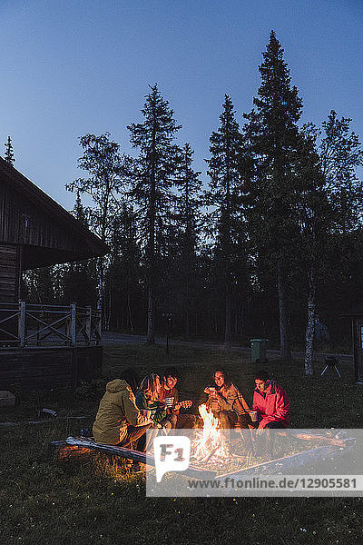 Group of friends sitting at a campfire  talking and drinking tea