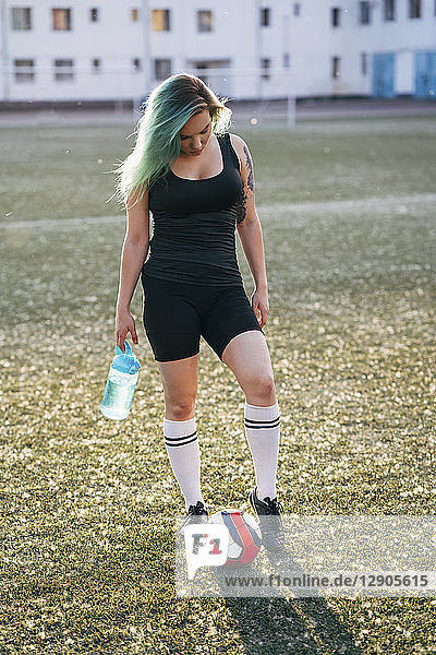 Young woman standing on football ground with ball and bottle of water