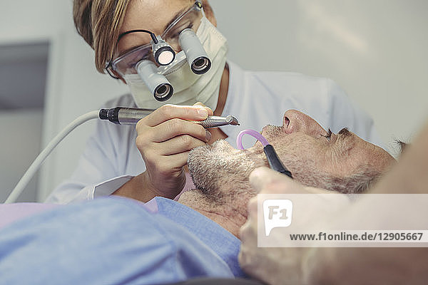Patient getting dental treatment  dentist using dental drill and head magnifiers and light