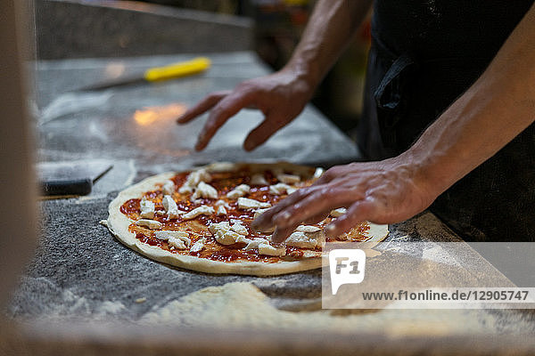 Close-up of pizza baker preparing a pizza with tomato sauce and mozzarella in kitchen