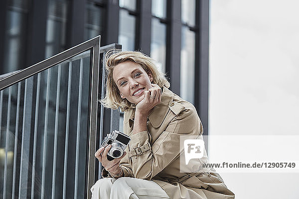Portrait of smiling blond woman with digital camera sitting on stairs