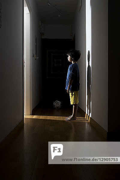 Lonely little boy standing in the corridor at home looking at open door