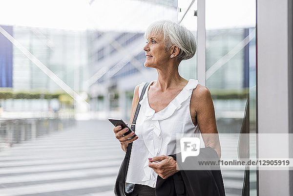 Senior woman with cell phone in the city looking around