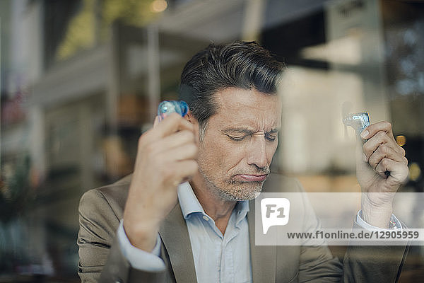 Mature businessman sitting in coffee shop  holding mini fans