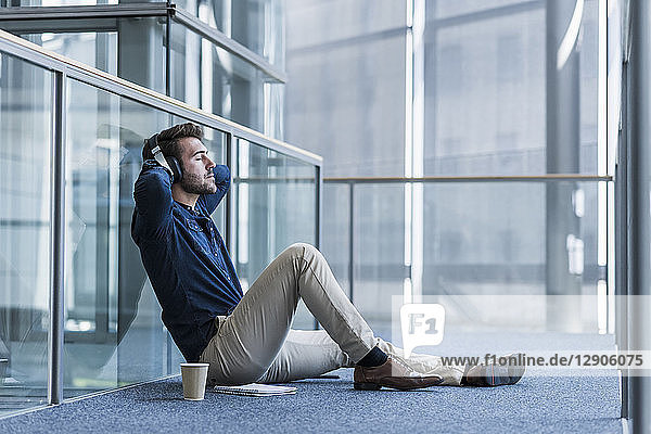 Businessman with headphones sitting on the floor relaxing