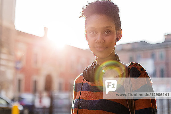 Portrait of smiling young woman with headphones at backlight