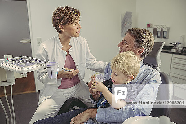 Female dentist talking to patient with son sitting on his lap