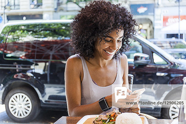 Portrait of smiling young woman with sitting at pavement restarant looking at cell phone