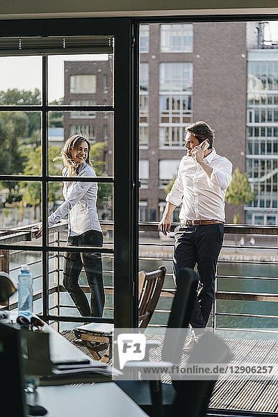 Businessman and woman standing on balcony  man making a phone call