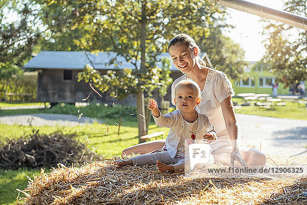Happy mother and little daughter playing with straw on a farm