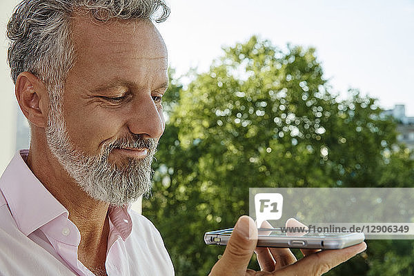 Portrait of smiling mature man holding smartphone outdoors
