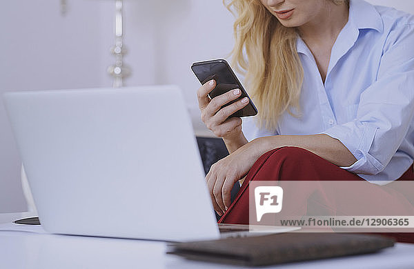 Blond woman sitting on couch  using laptop and smartphone