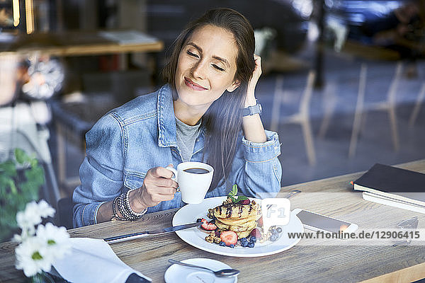 Smiling young woman enjoying pancakes and coffee in cafe