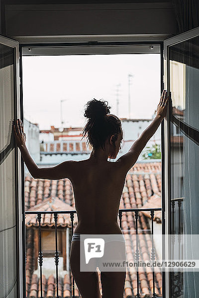 Beautiful barechested young woman standing at balcony door