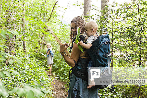 Woman hiking in the woods showing large leaf to baby boy in backpack