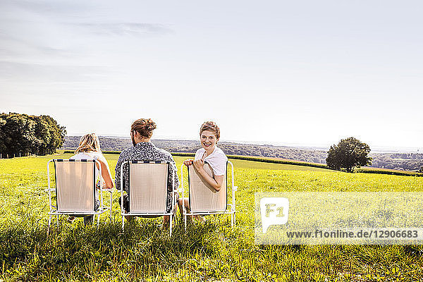 Friends sitting on camping chairs in rural landscape