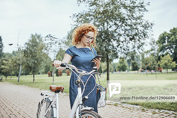 Young woman walking in park  pushing bicycle