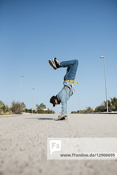 Trendy man in denim and cap skateboarding  standing on skateboard upside down