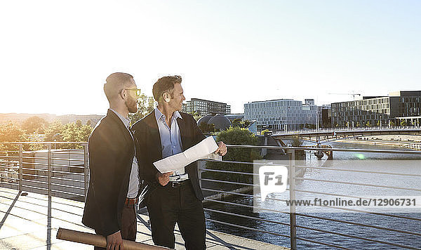 Two architects with blueprint standing on a bridge in the city